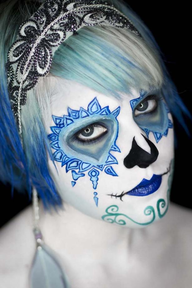 Eine Frau mit blau gefärbten Haaren und einem kunstvollen, blau-weißen Make-up im Stil von „Dia de los Muertos“.