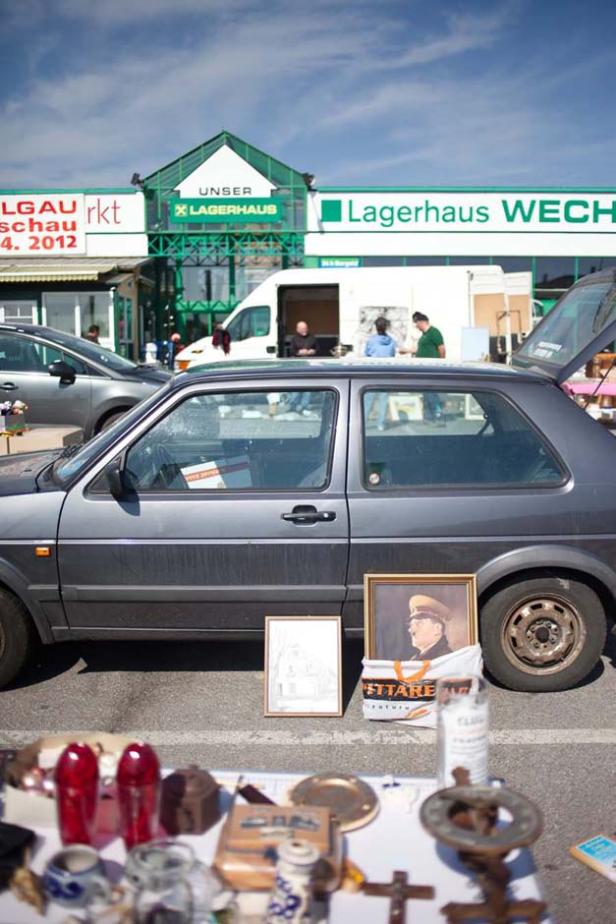 Auf einem Flohmarkt werden Bilder und Trödel neben einem Auto angeboten.
