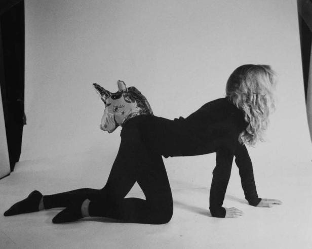 Eine Frau in schwarzer Kleidung kniet mit einer Einhornmaske auf dem Rücken.