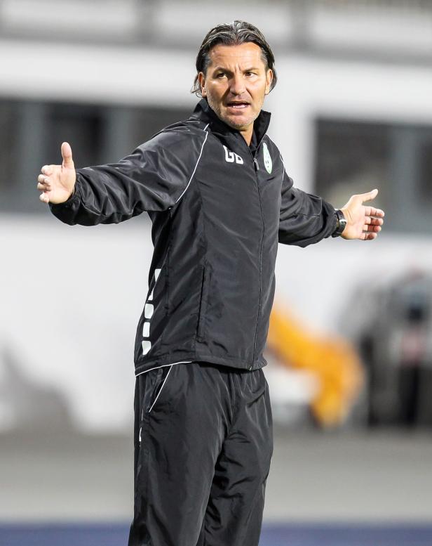 Ein Fußballtrainer gestikuliert während eines Spiels am Spielfeldrand.