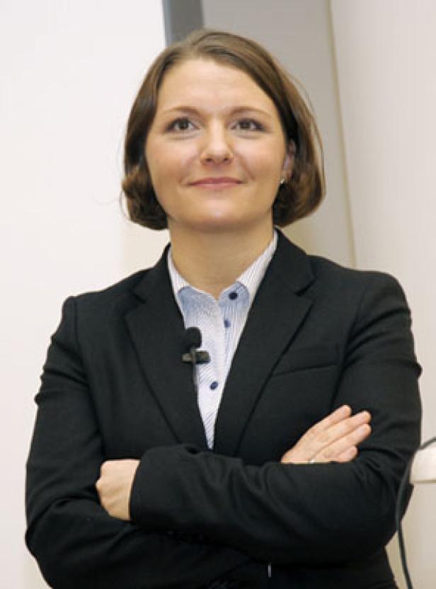 Eine Frau mit verschränkten Armen trägt ein schwarzes Jackett und ein hellblaues Hemd.
