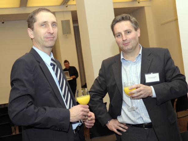 Zwei Männer in Anzügen halten Gläser mit Orangensaft in einem Konferenzraum.