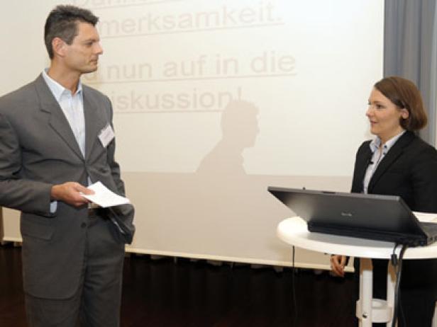 Ein Mann und eine Frau stehen vor einer Leinwand mit Text und diskutieren.