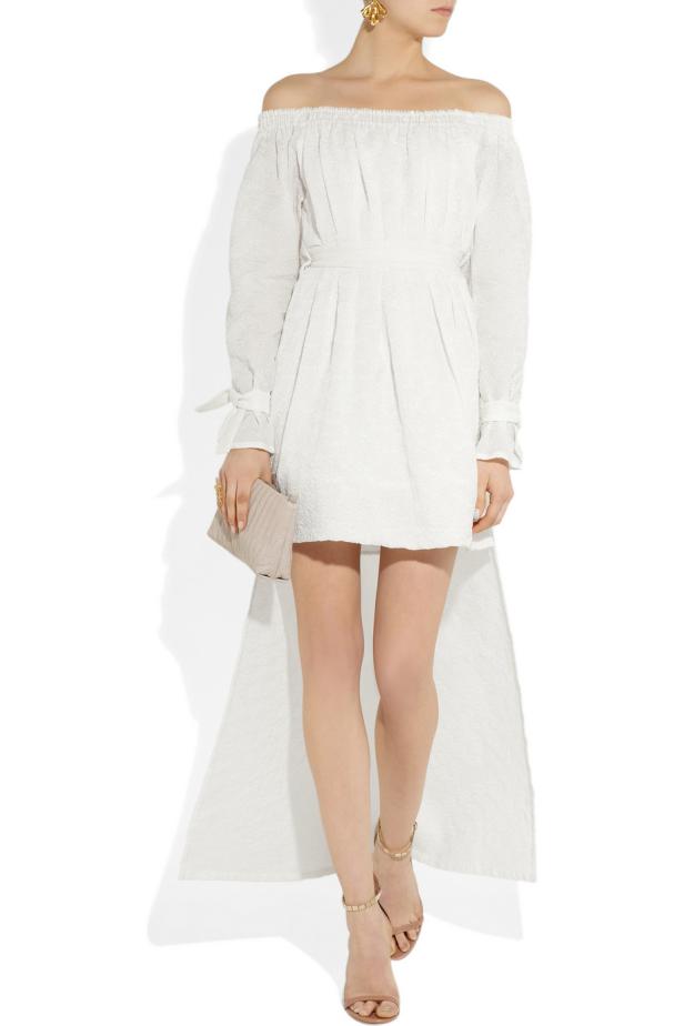 Eine Frau trägt ein weißes, schulterfreies Kleid mit Schleifen an den Ärmeln und Sandalen.