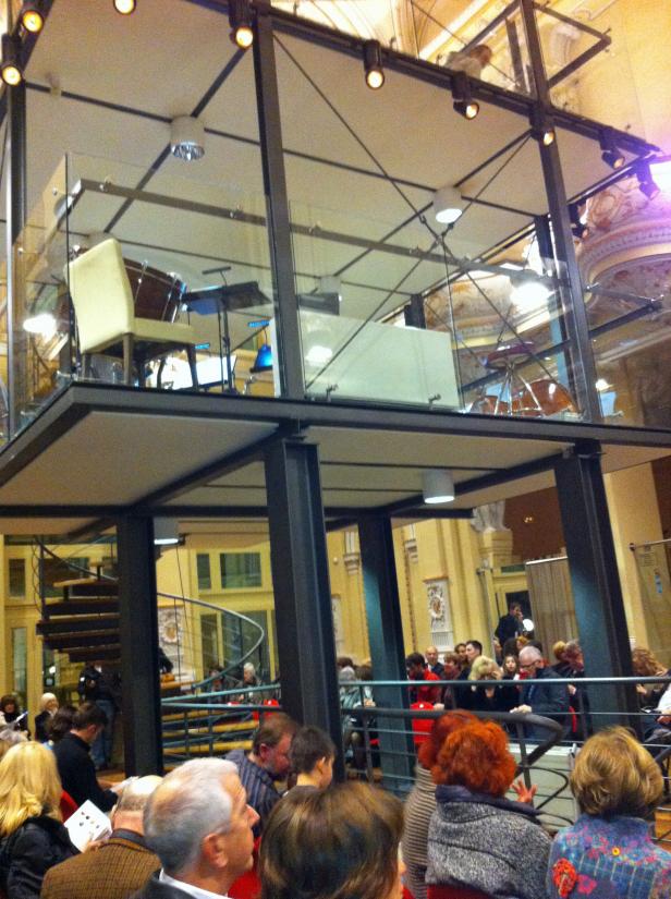 Zuschauer blicken auf eine Bühne in einem zweistöckigen Stahlgerüst.