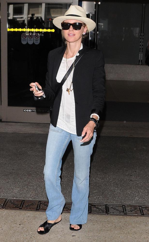 Naomi Watts mit Hut, Sonnenbrille und Jeans vor einem Gebäude.