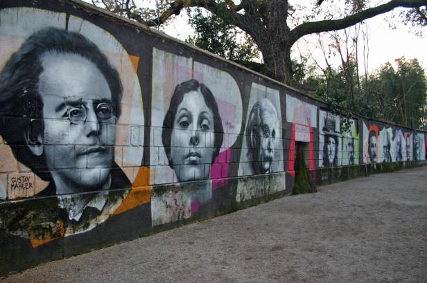 Eine Mauer mit Porträt-Graffiti von Gustav Mahler, Isadora Duncan und anderen Persönlichkeiten.