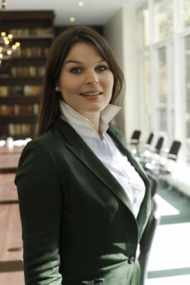 Eine Frau in einem grünen Blazer und weißem Hemd steht in einem Büro.