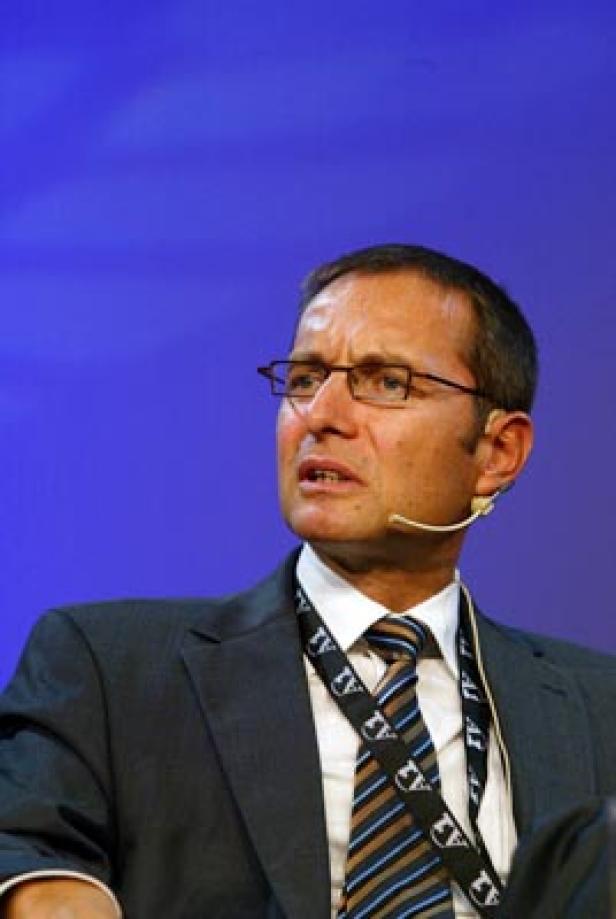 Ein Mann mit Brille und Anzug spricht vor einem blauen Hintergrund.