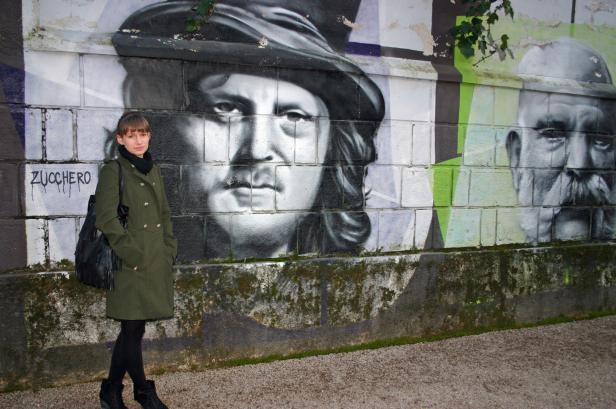 Eine Frau steht vor einer Wand mit Graffiti-Porträts.