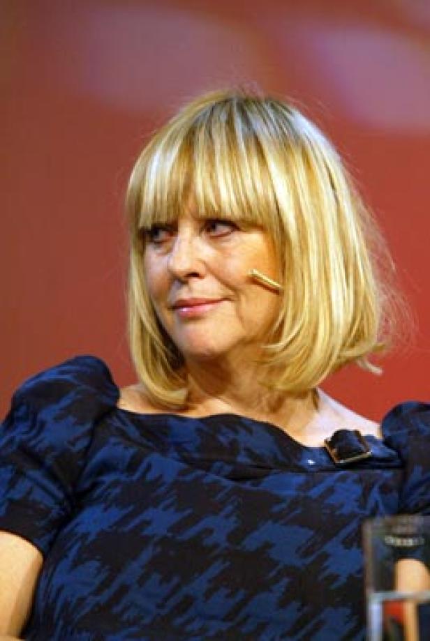 Eine Frau mit blonden Haaren und Pony trägt ein blaues Kleid mit Hahnentrittmuster.