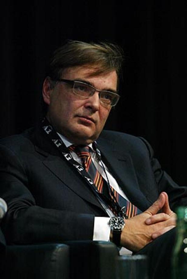 Ein Mann mit Brille und Anzug sitzt mit verschränkten Händen da.