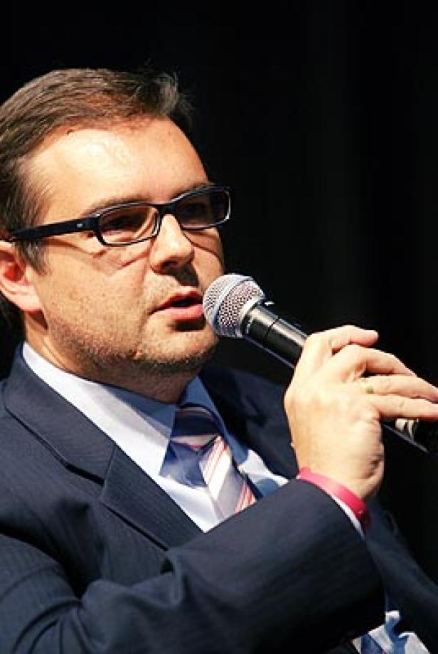 Ein Mann mit Brille und Anzug spricht in ein Mikrofon.