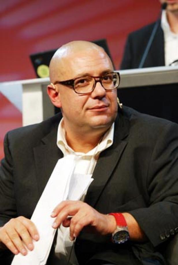 Ein Mann mit Brille und Anzug hält Papier in der Hand.