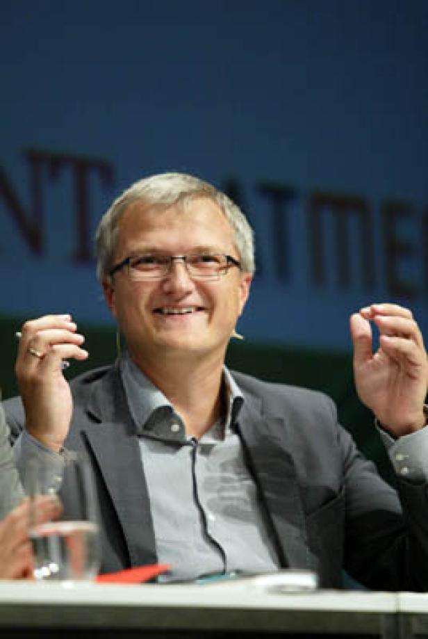 Ein Mann mit Brille gestikuliert bei einer Podiumsdiskussion.