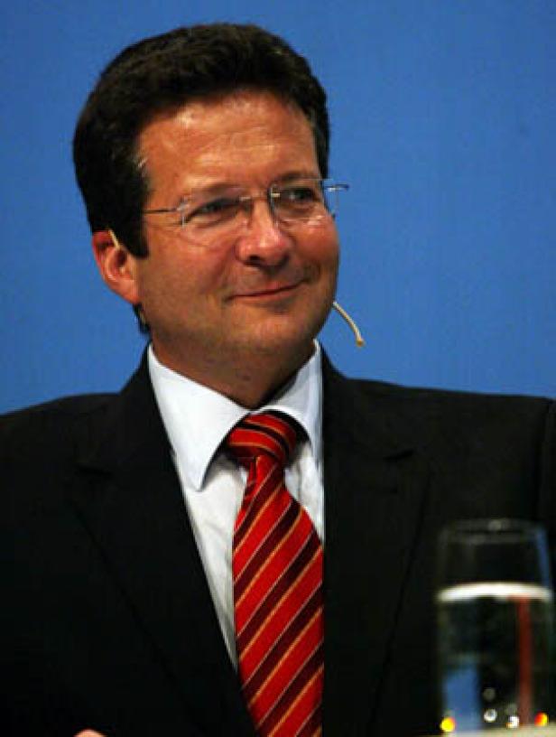Ein Mann mit Brille, Anzug und Krawatte lächelt.