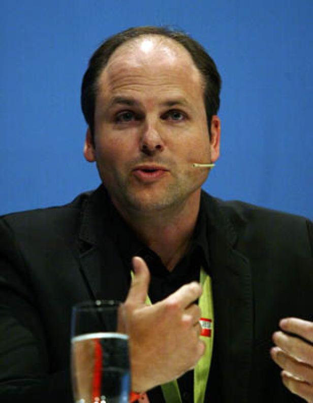Ein Mann mit Mikrofon gestikuliert während einer Präsentation.
