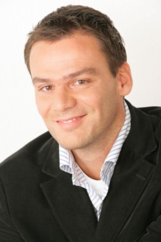 Ein lächelnder Mann in einem dunklen Cordjackett und einem gestreiften Hemd.