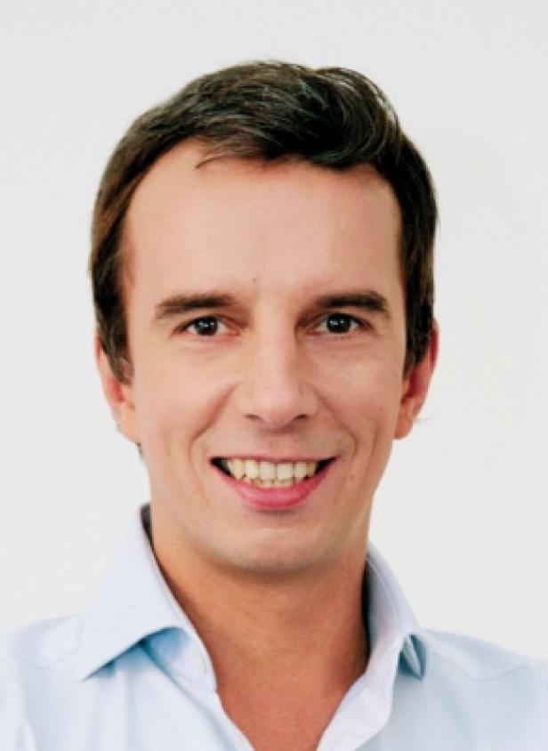 Ein lächelnder Mann mit braunen Haaren und einem hellblauen Hemd.