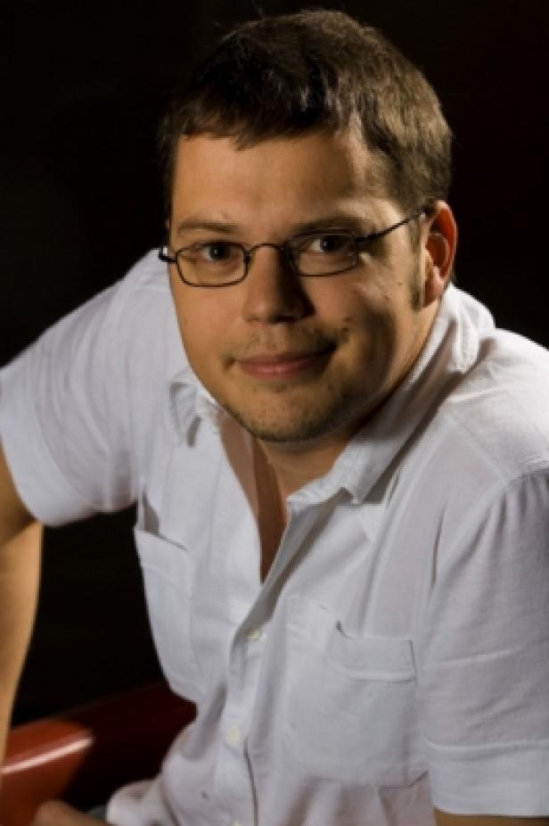 Ein Mann mit Brille und weißem Hemd lächelt in die Kamera.