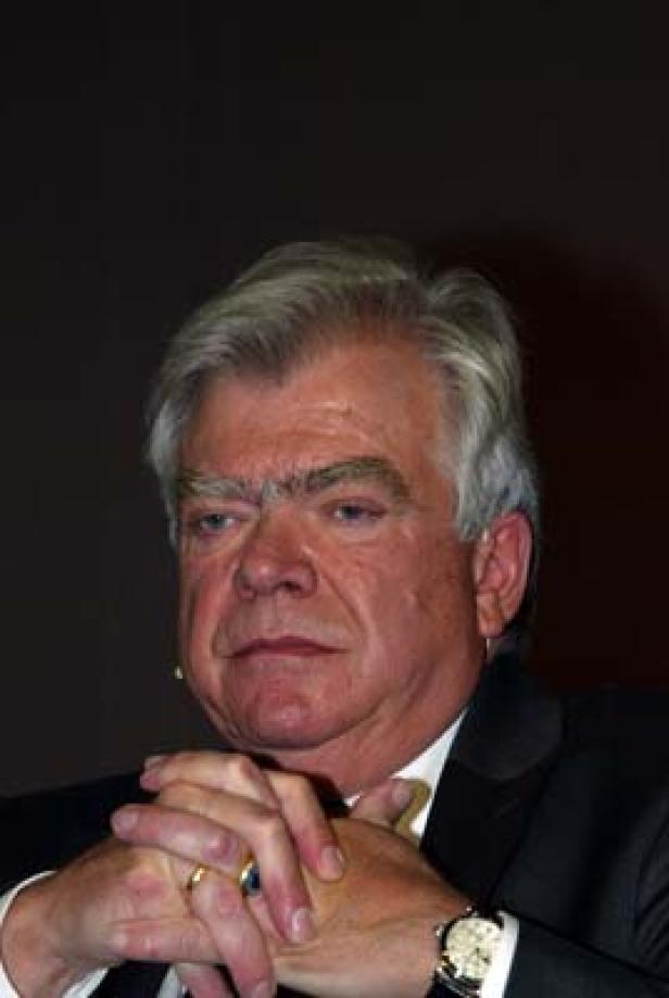 Ein Mann mit grauem Haar und Anzug verschränkt die Hände vor der Brust.