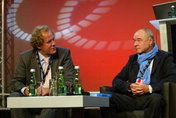 Zwei Männer sitzen auf einer Bühne und diskutieren.