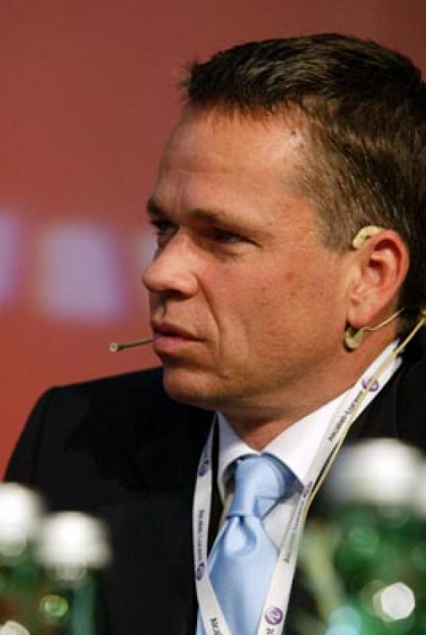 Ein Mann mit Anzug und hellblauer Krawatte trägt ein Headset.