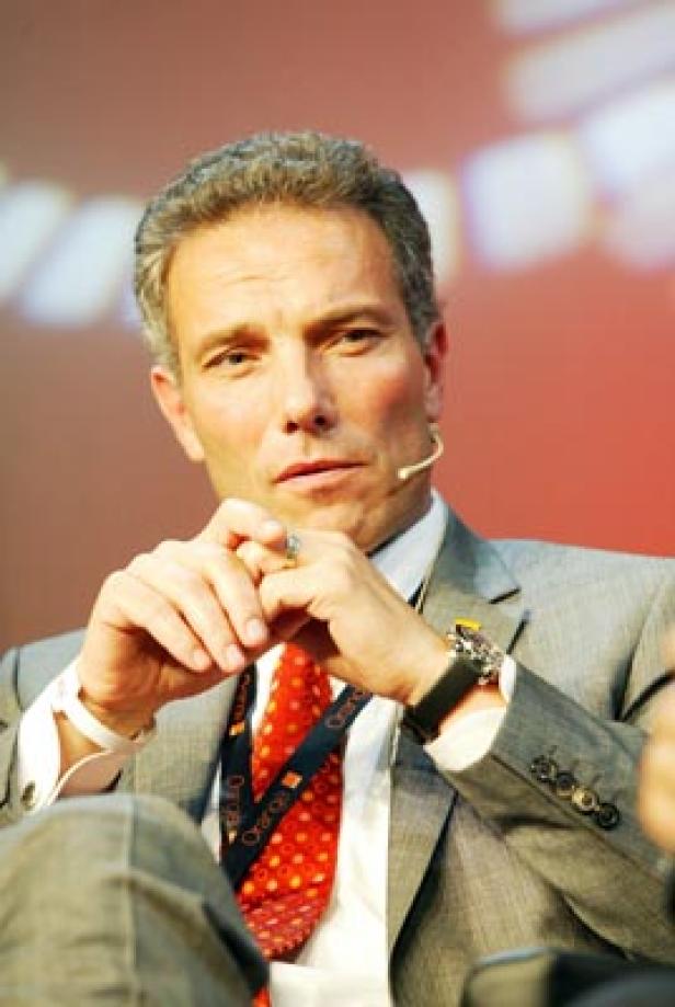 Ein Mann mit grau meliertem Haar, Anzug und Krawatte sitzt auf einem Podium.