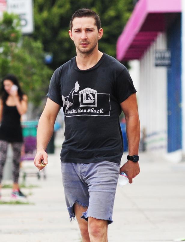 Shia LaBeouf in zerrissenen Jeansshorts und einem T-Shirt von „Chicken Shack“ geht die Straße entlang.