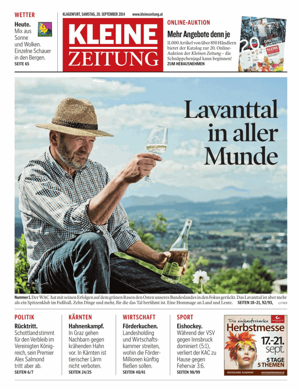Ein Mann mit Hut hält ein Glas Wein vor einer Landschaft im Lavanttal.