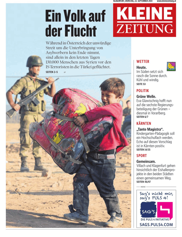 Ein Kind trägt eine große Tasche, während ein Soldat im Hintergrund steht.