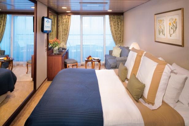 Ein Kabinenraum auf einem Kreuzfahrtschiff mit Bett, Sofa und Meerblick.