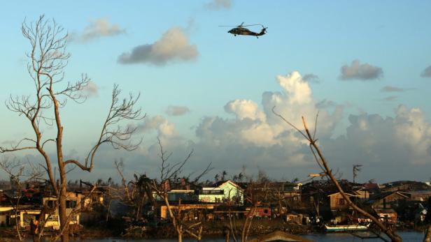 Ein Hubschrauber überfliegt ein zerstörtes Dorf nach einem Sturm.
