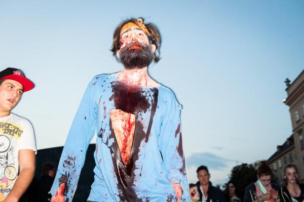 Ein Mann mit Bart und blutigem Make-up, möglicherweise ein Zombie, steht im Freien.