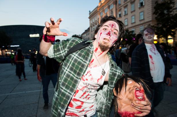 Ein Mann, als Zombie verkleidet, hält einen abgetrennten Kopf in der Hand.