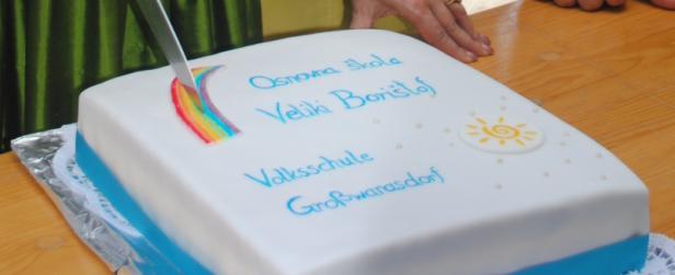 Eine Torte mit der Aufschrift „Osnovna škola Veliki Borištof Volksschule Großwarasdorf“ wird angeschnitten.