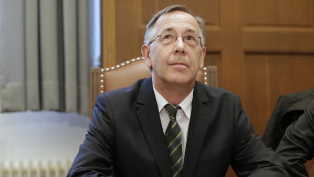 Ein Mann mit Brille und Anzug sitzt an einem Tisch.