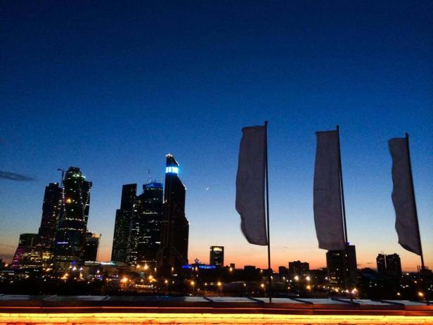 Die Skyline von Moskau erstrahlt im Abendlicht, flankiert von wehenden Fahnen.