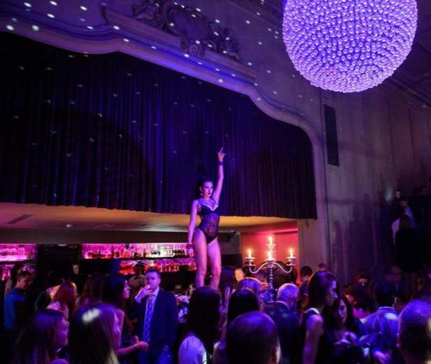 Eine Frau in einem schwarzen Body tanzt auf einer Bühne vor Publikum in einem Nachtclub.