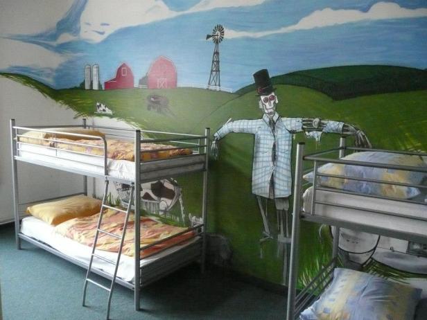 Ein Zimmer mit Etagenbetten vor einer Wandmalerei mit einer ländlichen Szene und einer Vogelscheuche.