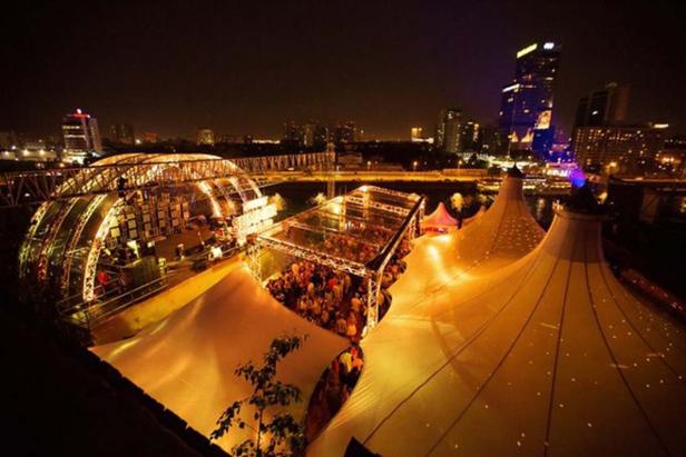 Blick auf eine abendliche Veranstaltung mit Zelten und Bühnen vor einer Stadtkulisse.