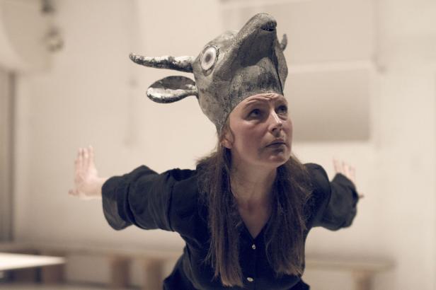 Eine Frau mit einer Tiermaske auf dem Kopf steht mit ausgestreckten Armen da.