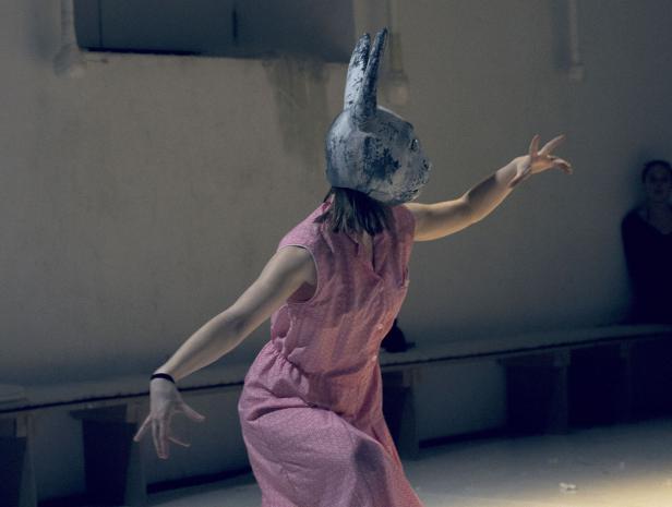 Eine Person mit Hasenmaske und rosa Kleid führt eine Performance auf.