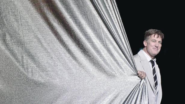 FOTOPROBE: "DIE DREIGROSCHENOPER" Ein Mann im Anzug zieht einen silbernen Vorhang zur Seite.