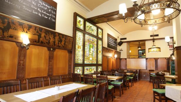 Innenansicht eines traditionellen Restaurants mit Holztäfelung und Buntglasfenstern.