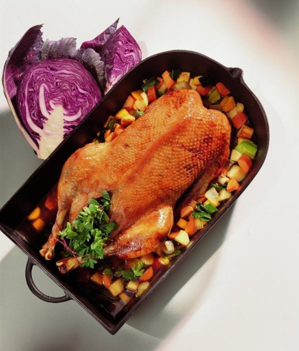 Ein gebratene Gans liegt in einer Bratform, garniert mit Gemüse und Rotkohl.