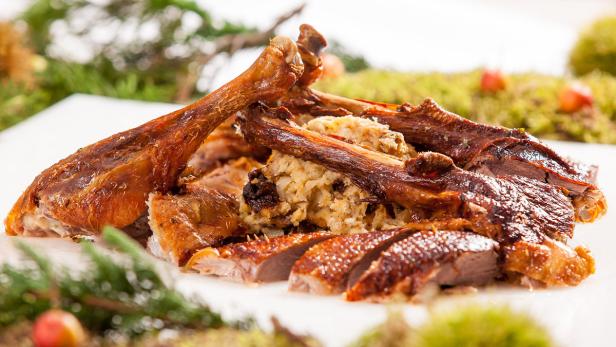 Ein tranchierter, gefüllter Braten liegt auf einer Platte, garniert mit Tannenzweigen.