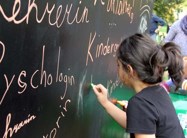 Ein Mädchen schreibt mit Kreide das Wort „Kindergarten“ auf eine Tafel.