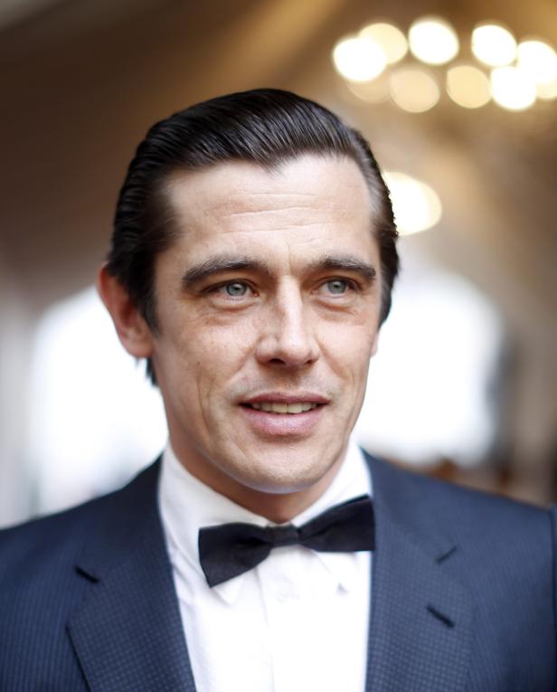 Ein Mann mit Fliege und dunklem Anzug blickt in die Ferne.