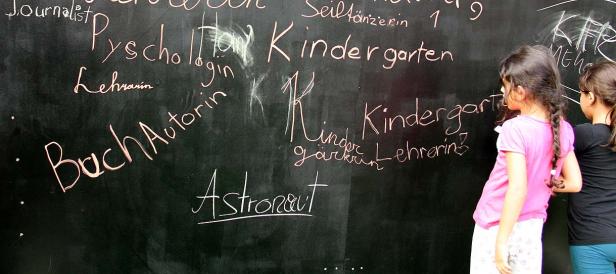 Zwei Mädchen schreiben Berufe wie „Kindergärtnerin“ und „Astronaut“ an eine Tafel.